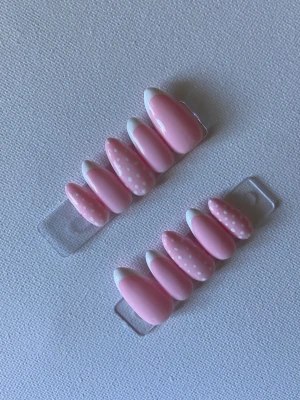 Rosa press-on naglar med prickar - Snygga press-on naglar i ljusrosa med vita prickar och fransk tipp. Mix av enfärgade och mönstrade naglar i mandelform. Perfekt för dig som vill ha en söt och trendig look. Lätta att applicera och ta bort.