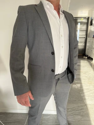 Grå kostym - aldrig använd  - Säljer en stilren grå kostym från H&M. Aldrig använd, endast testad hemma – i princip nyskick.  OBS: Olika storlekar  * Kavaj: 48 * Byxor: 50  Sitter snyggt och ger en modern, clean look. Passar extra bra om du har lite bredare underdel och smalare överkropp.  * Färg: Ljusgrå * Passform: Slim fit * Skick: Perfekt, inga fläckar eller skador  Bra kvalitet och fina detaljer både utvändigt och invändigt. Perfekt till student, jobb eller fest.  Säljes som set. Kan skickas direkt.