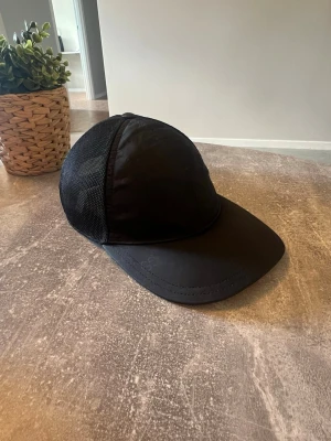 Svart keps från Gucci med mesh - Snygg svart keps från Gucci med diskret GG-mönster på framsidan och meshpaneler på sidorna för extra ventilation. Böjd skärm och justerbar passform. Perfekt accessoar för en trendig streetstyle-look.