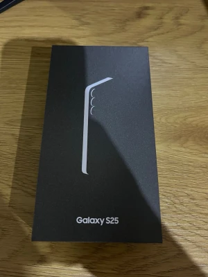 Samsung Galaxy S25 Android mobil - Samsung Galaxy S25 är en modern Android-telefon med stilren svart förpackning. Lådan visar en elegant design med flera kameror på baksidan. Perfekt för dig som vill ha en kraftfull smartphone med snygg look och avancerade funktioner.