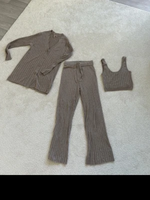 Beiges ribbat loungewear-set i tre delar - Mysigt loungewear-set i beige ribbat material med lång kofta, byxor  och matchande  top. Setet är supermjukt mot huden.