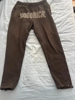 Svarta mjukisbyxor från Hoodrich - Mjukisbyxor i svart från Hoodrich med vit logotyp framtill. Byxorna har elastisk midja och smal passform med muddar vid benslut. Perfekta för chill eller streetwear-stil. Materialet är mjukt och bekvämt, idealiskt för att hänga med kompisar.