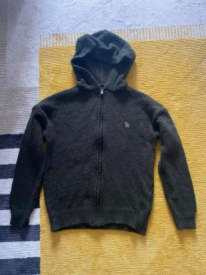 stickad hoodie  - Mysig mörkgrön stickad hoodie med dragkedja framtill och huva. Liten broderad detalj på bröstet. Långärmad och ribbade muddar vid ärmslut och nederkant. Perfekt för att hålla sig varm och ändå se chill ut. Storleken är xs men sitter som S och har en chill lite regular/baggy stil, aldrig använt den är helt ny.