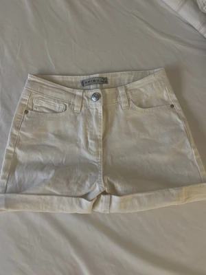 Vita high waist shorts från Amisu - Snygga vita shorts från Amisu med hög midja och klassisk femficksdesign. De har uppvikta benslut och stängs med knapp och dragkedja. Perfekta för varma dagar och enkla att matcha med olika toppar. Är en liten fläck men de går o få bort 🤗