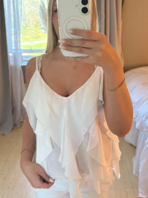 Vit volangtop från Zara - Superfin vit linnetopp från Zara med tunna axelband och flera lager volanger. Toppen har v-ringning och är perfekt för en fräsch och somrig look. Lätt och luftig i materialet. Storlek L men passar S/XS
