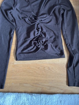 Brun ribbad topp från BikBok - Snygg brun långärmad topp från BikBok i ribbat material. Toppen har v-ringning och coola knutdetaljer framtill som ger en unik look. Perfekt att styla med jeans eller kjol för en trendig outfit.