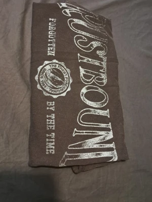 Dusty black oversized topp med tryck  - Dusty black topp från H&M med stort vitt tryck på bröstet där det står 'RUSTBOUND'. Rund halsringning och avslappnad passform. Perfekt för dig som gillar streetstyle och vill ha något unikt i garderoben.