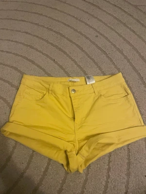 Gula lågmidjade shorts - Snygga gula shorts med låg midja och klassisk femficksdesign. Tillverkade i mjuk jeans med uppvikta benslut och knappstängning framtill. Perfekta för soliga dagar och enkel att matcha med olika toppar.