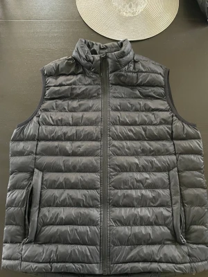 Svart dunväst från Everest - Snygg svart dunväst från Everest med hög krage och dragkedja framtill. Västen har två sidofickor med dragkedja och quiltad design som ger en sportig look. Perfekt för lager-på-lager och enkel att matcha till olika outfits.