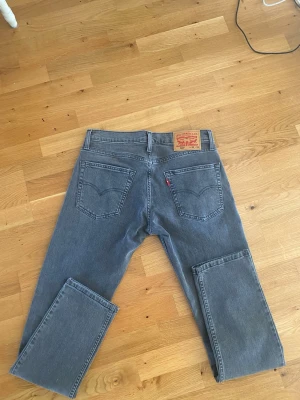Grå Levi's 501 jeans raka ben - Säljer ett par klassiska grå Levi's jeans med raka ben och femficksmodell. Jeansen har den ikoniska läderpatchen bak i midjan och röd Levi's-tagg på bakfickan. Perfekta för en avslappnad och stilren look. Storlek 30 w och 32 L 