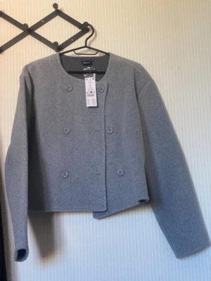 Grå dubbelknäppt kavaj - Stilren grå kavaj från Monki med dubbelknäppning och rund halsringning. Rak, boxig passform och långa ärmar. Tillverkad i ett mjukt tyg som ger en modern look. Perfekt för dig som gillar minimalistisk stil.