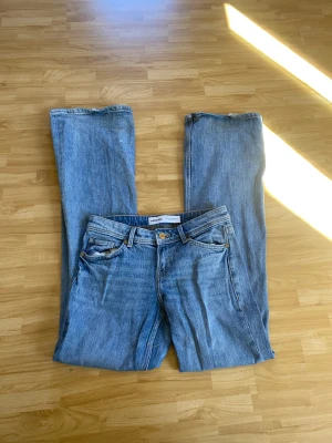  bootcut/raka  jeans från Bershka - Säljer ett par klassiska blå bootcut jeans från Bershka. Jeansen har fem fickor, gylf med dragkedja och knapp. Tillverkade i denim med en avslappnad passform och utsvängda ben. Kolla bild 4-6 för defekter. Lite slitna nertill och missfärgning på ena bakfickan 