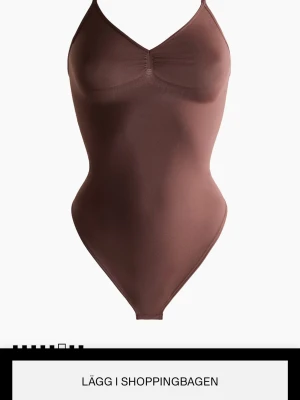 Brun body H&M - Säljer en stilren brun body med smala axelband och lätt rynk vid bysten. Bodyn har en enkel, figurnära passform och är tillverkad i ett mjukt, stretchigt material som sitter bekvämt mot kroppen.