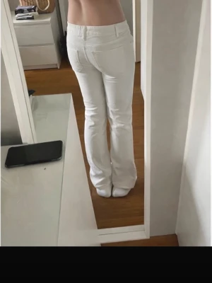 Vita bootcut jeans - Säljer ett par vita bootcut jeans i mid waist med klassiska fem fickor. Jeansen har utsvängda ben och stängs med knapp och dragkedja. Perfekta för dig som vill ha en clean och fräsch look. Innerbenslängden är 39,5cm och midjemåttet är 39cm