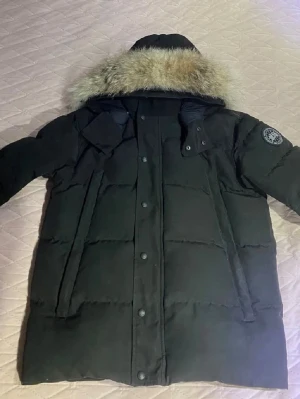 Canada Goose Black Label Wyndham Parka - Säljer en svart dunjacka av canada goose wyndham parka i black label i mycket bra skick. Man kan ta bort och sätta på pälsen. Den har 6 fickor och varm för kalla vinter dagar. Den är i storlek S men kan passa M också.