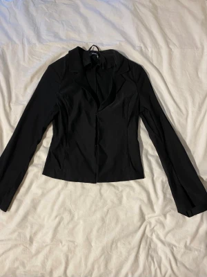 Svart figursydd topp - Stilren svart topp med figurnära passform och klassisk krage. Har långa ärmar och enkelknäppning framtill. Perfekt för en trendig och snygg look.