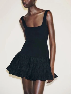 Svart volangklänning från Zara - Supersnygg svart kort klänning från Zara med breda axelband och fyrkantig ringning. Materialet är mjukt och stretchigt upptill och kjolen är i flera lager volanger