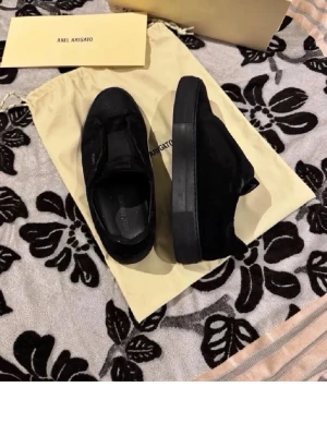 Svarta sneakers från Axel Arigato - Säljer ett par stilrena svarta sneakers från Axel Arigato i mocka. Skorna har en minimalistisk design med svart sula och diskret logga i guld på sidan. Perfekta för dig som gillar en clean och modern look.