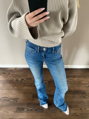 Blå bootcut jeans - Säljer ett par snygga blå bootcut jeans med låg midja och klassiska fem fickor. Jeansen har en lätt tvättad look och raka ben som går ut lite nedtill. Perfekta till sneakers eller boots för en avslappnad stil.