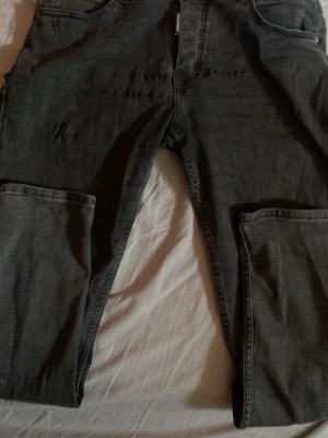 Svarta jeans från Dsquared2 - Säljer ett par svarta jeans från Dsquared2 med klassisk femficksmodell och rak passform. Jeansen är tillverkade i denim och har en diskret tvättad look som ger en cool vibe. Perfekta för dig som gillar streetwear och vill ha något stilrent. Det finns ett litet hål i byxorna men det går att sy. Priset kan diskuteras.