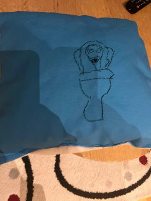 Blå kudde med Skibidi toilet - Gjorde detta mästerverk på syslöjden i skolan med statliga medel. Säljer nu denna eftersom att ekonomin går neråt, denna produkt är skapad men mycket kärlek och engagemang. Kvaliten och tyget är toppen (tror jag) Tog mig ca 8 timmar. Hoppas att någon köper denna kudde till ett billigt pris. Jag rekommenderar att använda den till att lägga huvudet på när man sover. Jag går 667,85 kr plus 