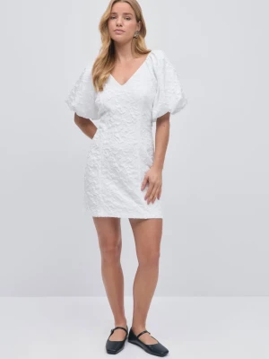 Vit kort klänning med puffärmar - Snygg vit kort klänning med v-ringning och stora puffärmar. Klänningen har ett subtilt strukturerat mönster i tyget och en figurnära passform. Perfekt för dig som vill ha en trendig och stilren klänning till exempelvis studenten! Klänningen är helt ny, lappen är borttagen då jag i sista sekund insåg att den inte passade mig och var tvungen att snabbt köpa en ny. 