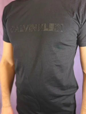 Svart t-shirt från Calvin Klein - Säljer en svart t-shirt från Calvin Klein med diskret logotyp i svart på bröstet. T-shirten har en klassisk passform och korta ärmar, perfekt för dig som gillar stilrena plagg med en modern touch. Materialet är mjukt och bekvämt bomull.
