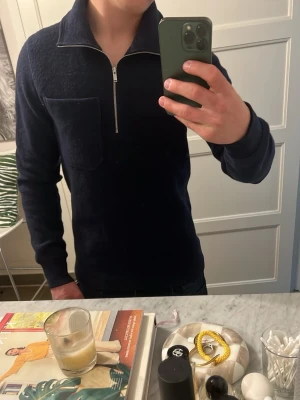 Mörkblå halvzip tröja - Mörkblå långärmad tröja med halv dragkedja och hög krage. Tröjan har en bröstficka och är tillverkad i ett mjukt, stickat material. Perfekt för en stilren och avslappnad look.