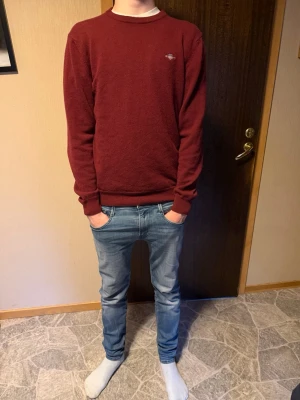 Mörkröd crewneck från Gant - Snygg mörkröd stickad tröja från Gant med rund halsringning och diskret logga på bröstet. Modellen är 182, skriv vid minsta fundering nypris 1400