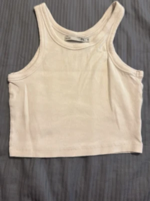 Vit ribbad crop top från 157 - Säljer en vit ribbad crop top från 157 med breda axelband och rund halsringning. Toppen är i ett mjukt och stretchigt material, perfekt för att styla med jeans eller kjol. Enkel och clean design som funkar till många outfits.