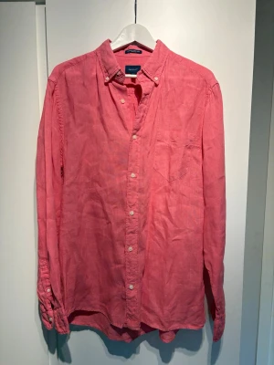 Rosa linneskjorta från Gant - Snygg rosa skjorta från Gant i linne med klassisk krage och knappar framtill. Skjortan har lång ärm och bröstficka, perfekt för en avslappnad men stilren look nu till sommaren. Storlek L!