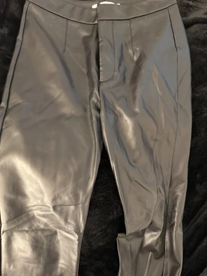 Svarta läderbyxor - Snygga svarta byxor i skinnimitation med hög midja och tight passform. De har en glansig yta som ger en cool look och är perfekta att styla med oversized tröjor eller crop tops. Materialet är stretchigt och följsamt för extra komfort.