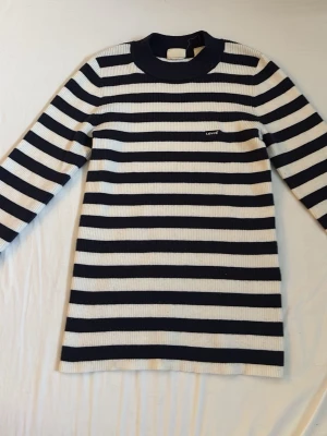 Randig stickad tröja från Levi's!! - Snygg stickad tröja från Levi's med marinblå och vita horisontella ränder. Tröjan har lång ärm, ribbstickad struktur och rund halsringning. Liten Levi's-logga på bröstet. Perfekt för en stilren och avslappnad look.