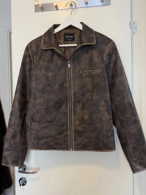 Brun skinnjacka från Ruishi - Snygg brun skinnjacka från Ruishi med klassisk krage, dragkedja framtill och tre fickor. Jackan har en cool vintage-look och raka ärmar med dragkedjor vid ärmsluten. Perfekt för dig som vill ha en stilren och tidlös jacka.  Jackan är aldrig använd, eftersom det ligger inflyttlåda så kommer jag tyvärr inte att skicka fler bilder. 