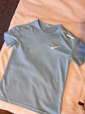 Ljusblå Nike t-shirt  - Snygg ljusblå t-shirt från Nike med klassisk logga på bröstet. Tillverkad i ett lätt och ventilerande funktionsmaterial som passar perfekt till träning. T-shirten har rund halsringning och korta ärmar för en sportig look. Är 173 och 65 kg 
