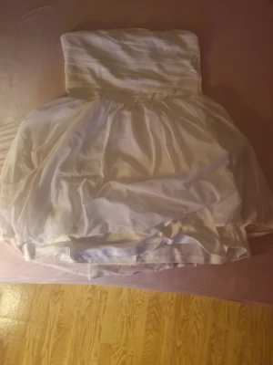 Vit axelbandslös klänning NLY Blush - Snygg vit axelbandslös kortklänning från NLY Blush. Klänningen har en puffig kjol och en tight överdel med draperad effekt. Perfekt för sommarens alla tillfällen. Tillverkad i ett lätt och luftigt material. Helt ny med prislapp. Priset kan diskuteras🫶🏼