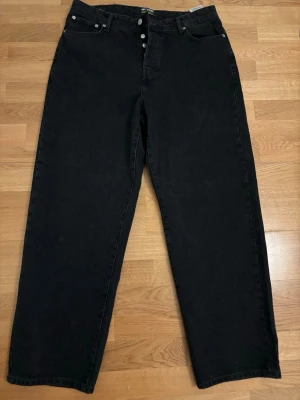 Svarta jeans från Only & Sons - Svarta raka jeans från Only & Sons med knappgylf och klassisk femficksdesign. Jeansen har en avslappnad passform och är tillverkade i denim. Perfekta för en stilren och enkel look.