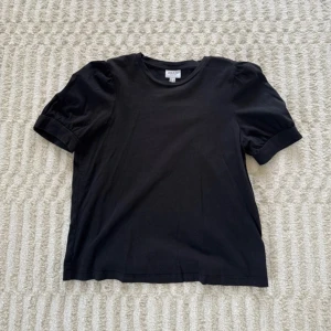 Svart topp med puffärm från Aware - Svart topp från Aware by Vero Moda med rund halsringning och korta puffärmar. Tillverkad i mjuk bomull, stilren design