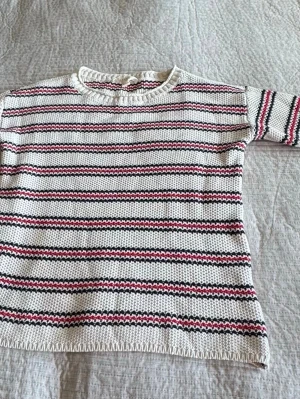 Randig stickad tröja från Esprit - Vit stickad tröja från Esprit med horisontella ränder i svart och rött. Tröjan har rund halsringning med ribbstickad kant och långa ärmar. Perfekt för en avslappnad och trendig look.