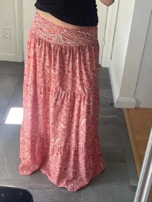 Rosa långkjol  - Säljer en bohemisk långkjol i rosa med vitt paisleymönster. Kjolen har en bred linning och faller snyggt ner mot golvet. Perfekt för dig som gillar en avslappnad och trendig stil.