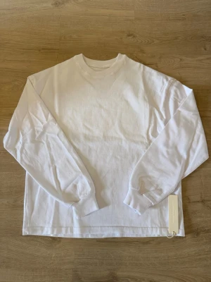 Vit långärmad tröja Velour Garments - Klassisk vit långärmad tröja från Velour Garments med rund halsringning och ribbade muddar. Tillverkad i mjukt bomullsmaterial för en clean och enkel look. Perfekt att styla lager på lager eller bära som den är. Helt ny endast testad på.