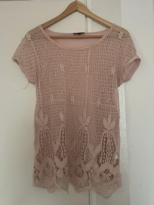 Beige spetsblus med kort ärm - Säljer en beige blus med korta ärmar och rund hals. Blusen har ett vackert spetsmönster framtill och är lätt transparent. Perfekt för dig som gillar romantiska detaljer och en feminin stil.