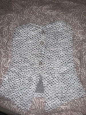 Vit -topp med knappar - Supersnygg vit -topp med strukturmönster och dekorativa pärlknappar framtill. Toppen är axelbandslös och har en liten slits framtill för extra edge. Perfekt att styla med jeans eller kjol för en trendig look. 