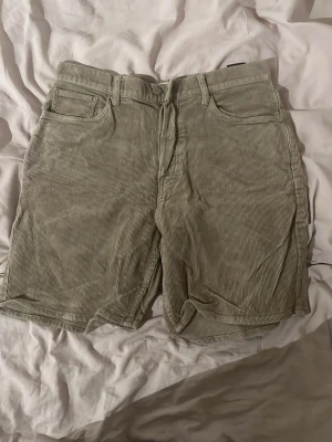Beiga manchester shorts från Weekday - Snygga beiga shorts i manchester från Weekday. Klassisk femficksmodell med bälteshällor och knappgylf. Perfekta för en chill och trendig look under varmare dagar.