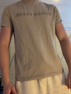 Beige t-shirt från Canada Goose - Snygg beige t-shirt från Canada Goose med broderad logga framtill. Klassisk passform med rund hals och korta ärmar. Perfekt för en stilren och avslappnad look.