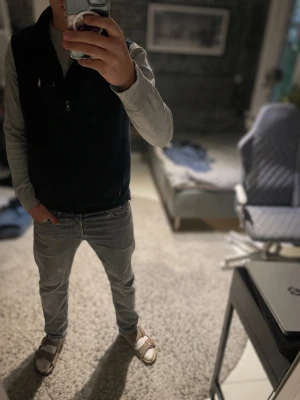 Mörkblå väst från Polo Ralph Lauren - Snygg mörkblå väst från Polo Ralph Lauren med dragkedja framtill, hög krage och tre fickor med dragkedja. Västen har en stilren design med liten logga på bröstet och justerbar nederkant. Perfekt att slänga över en hoodie eller tröja. Storlek M