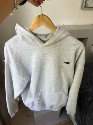 Ljusgrå hoodie från Urban Classics - Säljer en stilren ljusgrå hoodie från Urban Classics. Hoodien har en klassisk känguruficka framtill, huva och ett litet svart logomärke på bröstet. Tillverkad i mjukt sweatshirtmaterial som är perfekt för chill dagar.