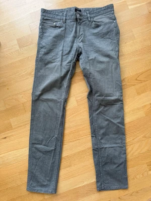 Gråa slim fit jeans från Hugo BOSS  - Snygga gråa slim fit jeans från Hugo BOSS med klassisk femficksdesign och dragkedjegylf. Jeansen har raka ben och är tillverkade i ett mjukt bomullsmaterial med lite stretch för extra komfort. Perfekta för en stilren och avslappnad look.