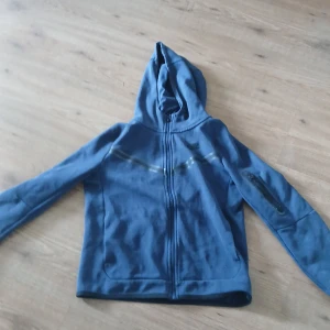 Nike tech - Säljer en blå hoodie från Nike i storlek L junior. Tröjan har huva, hel dragkedja framtill och en ficka med dragkedja på ena ärmen. Perfekt för dig som gillar sportig och avslappnad stil. Pris kan diskuteras.