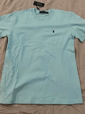 Ljusblå t-shirt från Polo Ralph Lauren - Säljer en ljusblå t-shirt från Polo Ralph Lauren, nyskick. Hör av vid frågor och funderingar!!